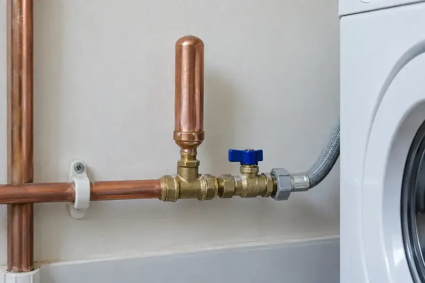 Copper water hammer arrestor fitted beside a washing machine supply valve.